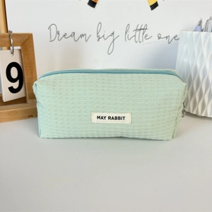 Detail of mint green waffle textured pouch with zipper closure and woven brand label