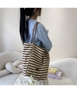 Détail du sac cabas en toile rayée montrant la vue latérale avec des anses en cuir marron