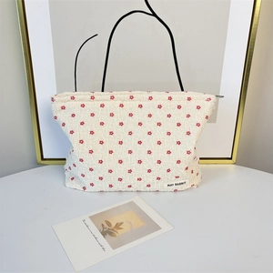 Detailed texture of seersucker makeup bag with red floral embroidery and brand label