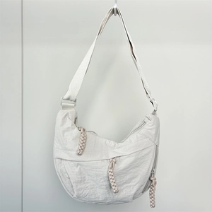 Detail of minimalist nylon dumpling bag showing pleated texture and rope zipper pulls