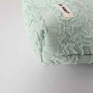 Detail of mint green puckered fabric texture and woven brand label on cosmetic bag