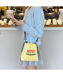 Detail of a yellow canvas crossbody bag with bakery embroidery and woven drawstring straps