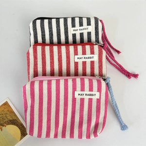 Three minimalist striped canvas coin purses with zippers and woven rope pulls in white background