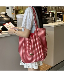 Detail of red checkered canvas tote bag with golden metal logo and long shoulder strap
