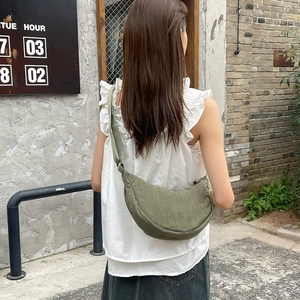Detail of dark green corduroy crescent crossbody bag showing texture and size on model