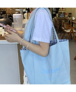 Detail of light blue canvas tote with blue plaid lining and Our fave letter print