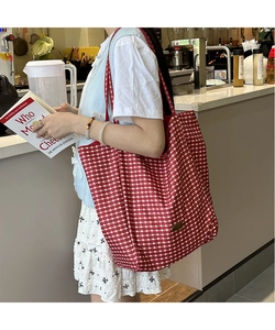 Detail of red and white checkered canvas tote bag with vintage metal plaque accent