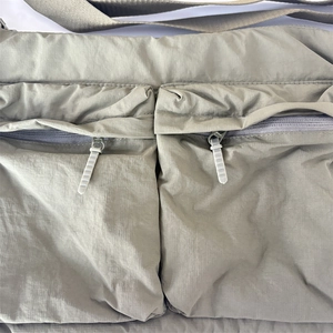 Détail du sac en nylon vert olive montrant deux poches zippées et texture durable