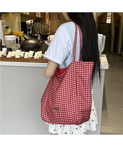 Side view of red and white checkered canvas tote bag with a circular metal brand label