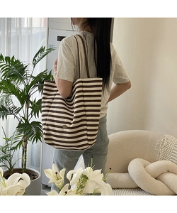 Sac cabas en toile rayée marron porté à l'épaule dans un décor d'intérieur douillet