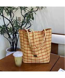 Close-up of yellow plaid canvas tote bag with woven handles on dark wooden table
