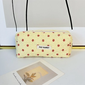 Detail of yellow seersucker makeup bag with red flower embroidery and zip closure