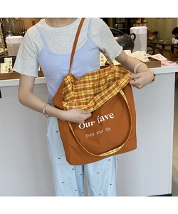 Detail of orange canvas tote bag with white lettering and yellow plaid reversible lining
