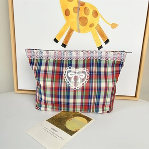 Detailed view of plaid cosmetic bag with white lace edges and heart ribbon embroidery