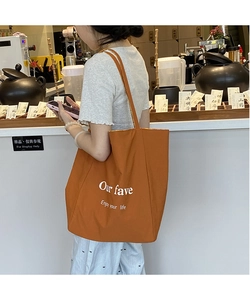 Detail of orange canvas tote bag with white lettering and reinforced shoulder strap