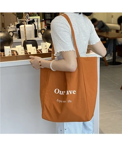 Macro detail of a large orange tote bag with white lettering against an urban cafe backdrop
