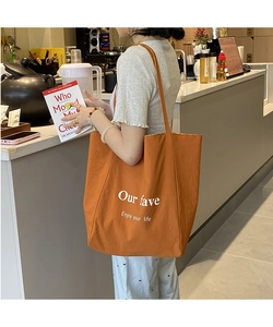 Detail of orange canvas tote bag with white 'Our fave' slogan in a cozy cafe setting
