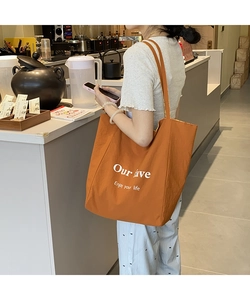 Orange canvas tote bag with white text print shown on shoulder in a cafe setting