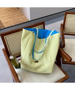 Close-up of a yellow plaid tote bag with blue contrast lining on a wooden chair