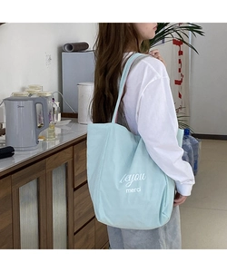 Vue détaillée du sac cabas en toile bleu clair avec l'inscription 'merci' portée