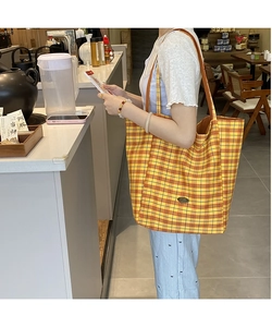Detail of yellow plaid canvas tote bag with long shoulder straps and metal logo plate