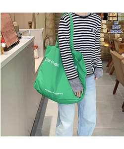 Green canvas tote bag detail featuring the white Low Classic logo and printed text