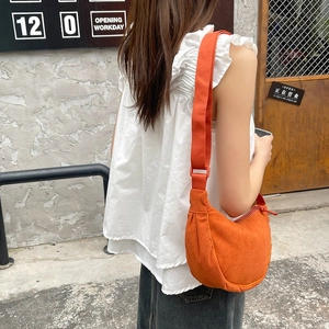 Detail view of orange corduroy texture and adjustable strap on a half-moon crossbody bag