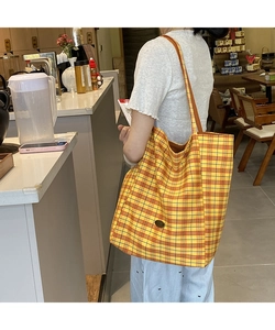 Detail showing a yellow tartan canvas tote bag worn by a model in a shop interior