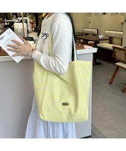 Detail of yellow checkered tote bag showing blue shoulder strap and side brand plaque