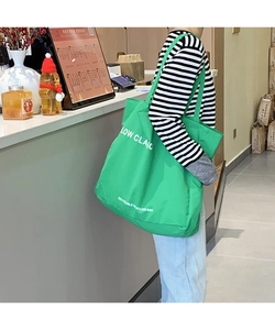 Detail of green canvas tote bag with white lettering worn over the shoulder by a model