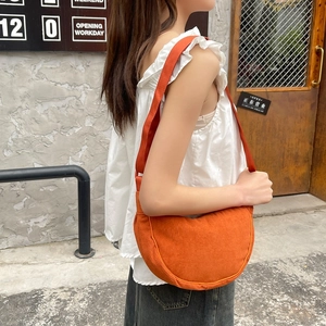 Detail view of orange corduroy crescent shoulder bag with ribbed texture shown in street style