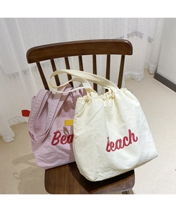 Detail of pink and white nylon tote bags with Beach print on a wooden chair