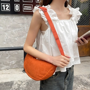 Detail view of a burnt orange corduroy crescent crossbody bag worn by a model in casual style