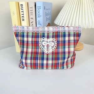 Close-up of tartan makeup bag with delicate white lace trim and heart-shaped bow patch
