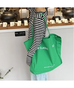 Green canvas tote bag featuring W CLASSIC letter print shown in a lifestyle street setting