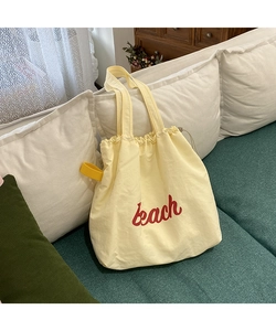 Detail of light yellow nylon tote bag featuring red Beach print and drawstring closure