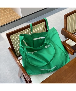 Detail of green canvas tote bag featuring white letter print on a vintage wicker chair