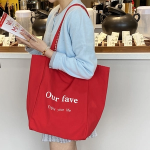 Large red canvas tote bag with white lettering and sturdy handles shown in lifestyle setting