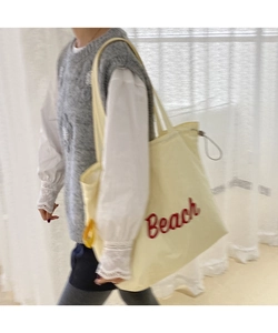Beige nylon tote bag with red Beach print shown being worn by a model in a soft room
