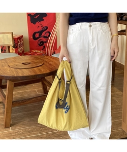 Close-up of vibrant yellow nylon tote bag featuring blue letter print and dual straps