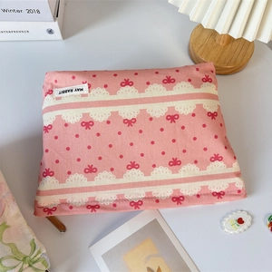 Close-up of pink canvas pouch with red bow and lace print on a minimalist desk