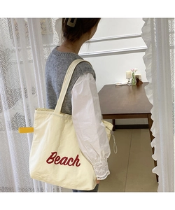 Detail of white nylon tote bag with red Beach print and yellow decorative strap on shoulder