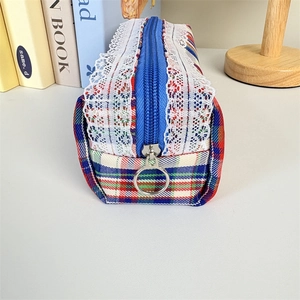 Detailed shot of striped plaid makeup bag with white lace trim and round metal zipper