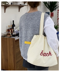 Close-up of off-white nylon tote bag with red embroidered 'Each' and yellow strap details