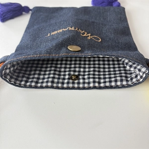 Detail of denim crossbody bag featuring vintage buckle, plaid lining, and purple tassel