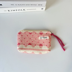 Detail of pink canvas pouch with red bow patterns, lace trim and woven wristlet strap