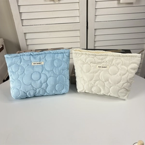 Detail of quilted floral cosmetic bags in light blue and beige with metal zipper closure