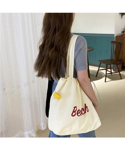 Detail of cream nylon tote bag with red Beach embroidery and yellow side label