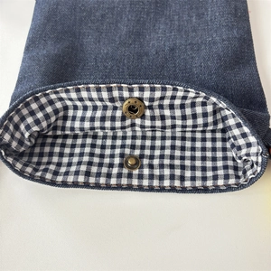 Detail of blue denim crossbody bag featuring a vintage star press stud and plaid lining