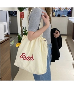 Detail of off-white canvas tote bag with red Bean embroidery and drawstring closure